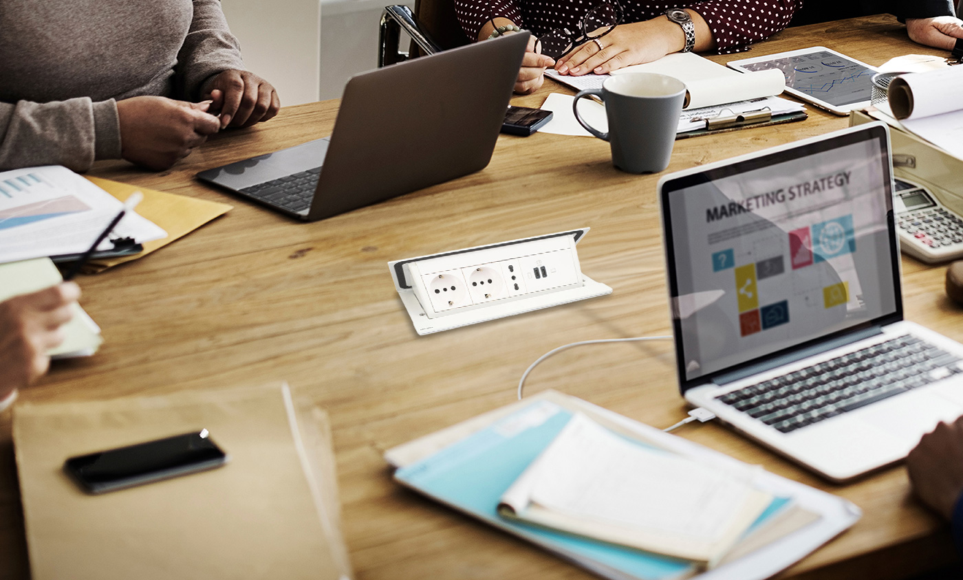 Delle persone utilizzano computer portatili sedute a un tavolo dotato di Torretta Pop-up 150482NW BTicino.