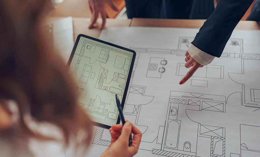 Due persone esaminano progetti architettonici e planimetrie su carta e tablet, discutendo i dettagli del layout.